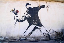 Jedno zz nejznámějších graffiti Love Is In The Air - maskovaný demonstrant házející kytici květin.